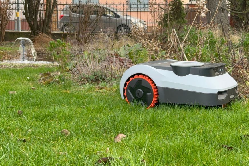 Segway Navimow i210 LiDAR Pro Mähroboter mit orangefarbenen AWD-Rädern navigiert selbstständig durch einen Garten mit Beeten und Bäumen ohne Begrenzungskabel